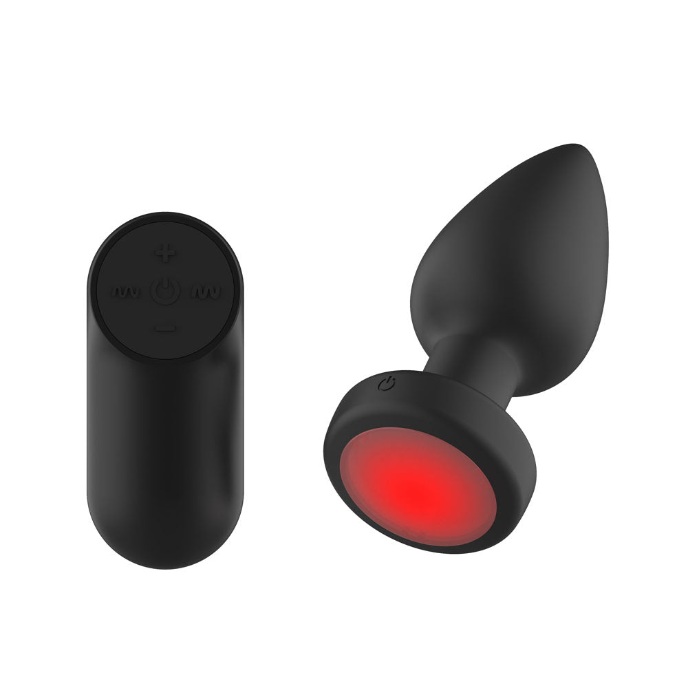 Passion Play medium black vibrating butt plug and wireless remote, angled to show the glowing red LED base